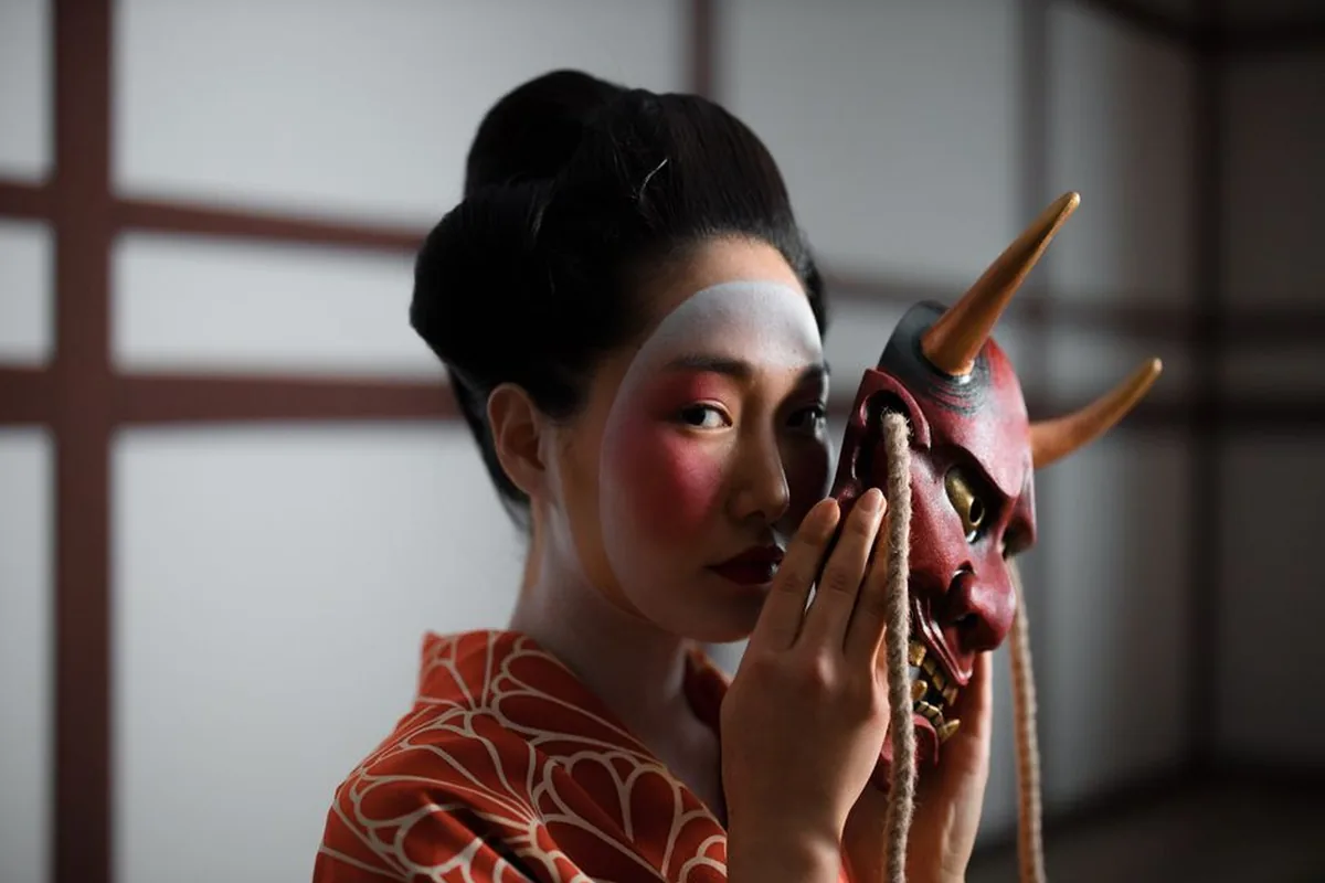 A performer in kimono holding a red horned mask of the kind used in Noh theatre, representative image